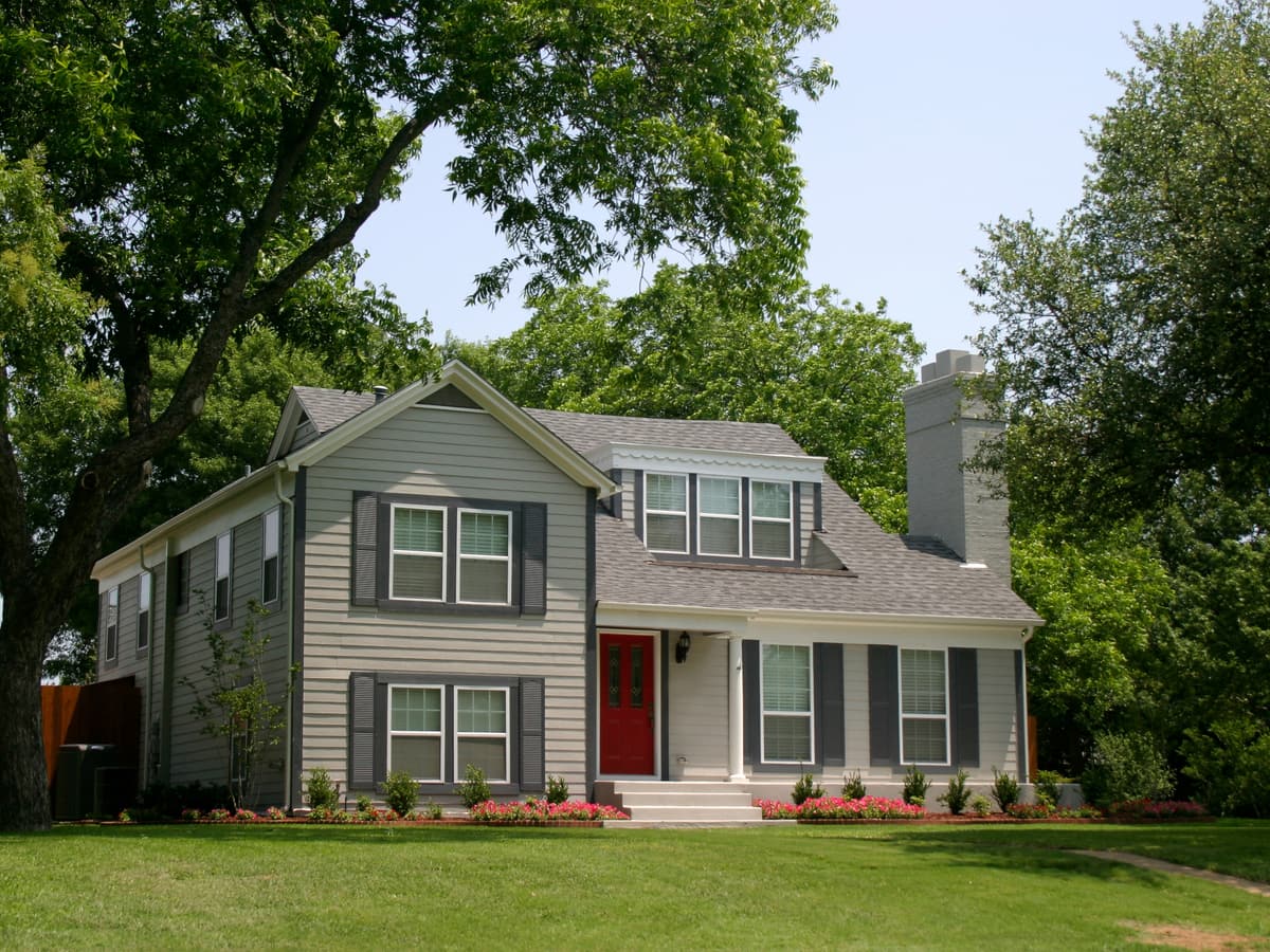 A two-story house with grey siding among mature trees