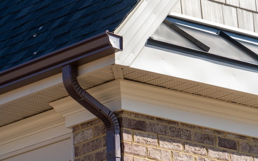 A dark seamless gutter and downspout on a brick house