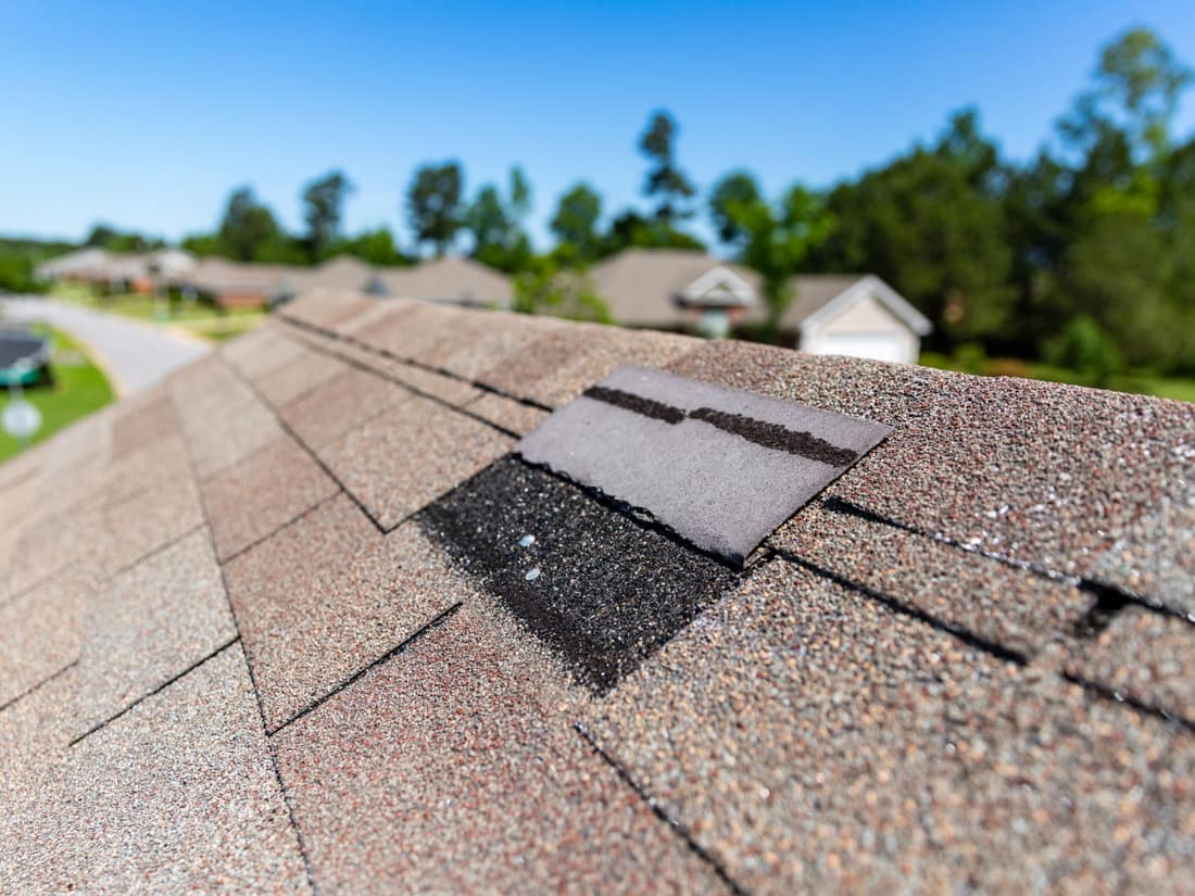 A lifted and cracked asphalt shingle, photographed close up on a roof